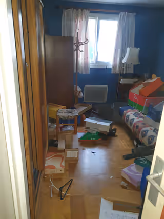 Chambre d’appartement encombrée de cartons, d’une armoire et d’objets posés au sol