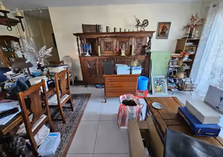 Séjour d’un logement ancien, buffet en bois, tableaux et objets accumulés avant le tri