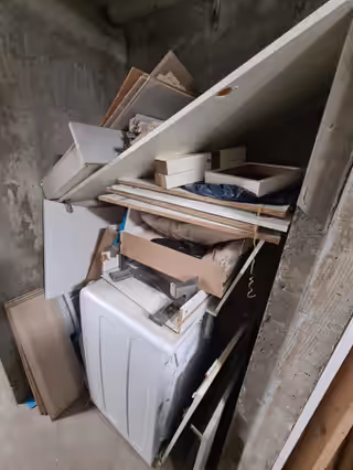 Cave en béton remplie de panneaux de meuble démontés et d’un lave-linge hors d’usage